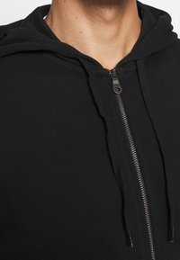 Černá mikina na zip z žebrované látky, s předním zipem, šňůrkami a přiléhavým střihem kolem krku.