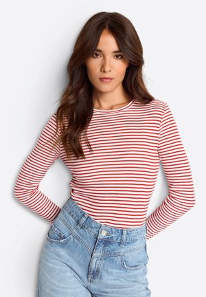 Langärmliges, Rundhalsoberteil mit rot-weißen horizontalen Streifen. Kombiniert mit hellblauen, hochtaillierten Jeans.
