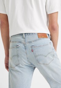 Světle modré džíny z denimu s klasickým střihem, které mají dvě zadní kapsy a koženou nášivku na pasu s logem značky.