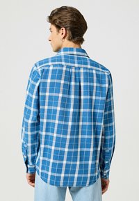 Blauw geruit shirt met een mix van lichtblauwe en donkerblauwe vierkanten, kraag, lange mouwen en knoopmanchetten. Gemaakt van een lichtgewicht stof.