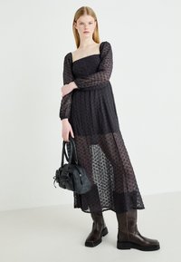Czarna przezroczysta sukienka z teksturowanej tkaniny, z długimi rękawami i kwadratowym dekoltem. Połączona z skórzanymi botkami do kolan i czarną torebką.