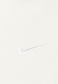 Vitt bomullstyg med en mjuk struktur som har en liten, broderad silverfärgad Nike swoosh-logotyp på vänster sida.