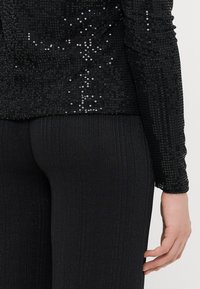 Czarny długi rękaw bluzka ozdobiona cekinami, połączona z prążkowanymi czarnymi spodniami. Bluzka ma teksturowany połysk i dopasowany krój.