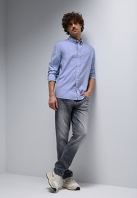 Light blue button-up shirt with long sleeves, gray jeans, and beige sneakers, against a gray background. Cotton material, relaxed fit.