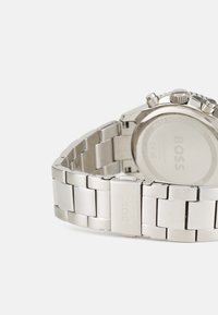 Montre en acier inoxydable argenté avec finition brossée, bracelet à maillons, boîtier circulaire et fonctionnalités de chronographe. Nom de la marque gravé sur le fermoir.