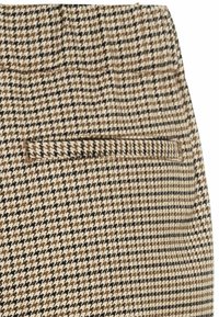 Tissu à motif pied-de-poule beige, noir et marron avec une poche passepoilée étroite sur un vêtement.