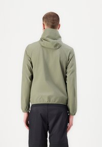 Chaqueta ligera verde oliva con capucha, puños elásticos y dobladillo. Textura suave con un corte casual, combinada con pantalones cortos negros.