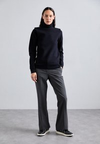 Marineblå turtleneck genser med en myk tekstur, kombinert med grå skreddersydde bukser. Svarte joggesko har en hvit såle og dekorative detaljer.