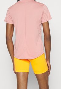 Top deportivo de manga corta en color rosa, combinado con shorts amarillos ajustados, fabricados con un tejido liso y elástico de corte clásico.