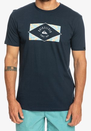 Navy blue cotton t-shirt featuring a diamond-shaped Quiksilver logo with floral accents in turquoise and orange, short sleeves, and a relaxed fit.
