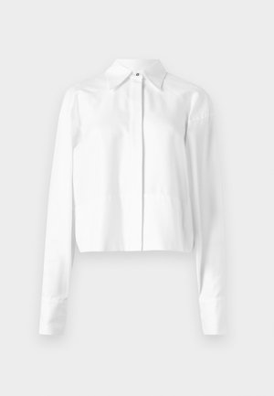 Camisa branca cropped com mangas longas, colarinho clássico e fecho frontal de botões. Feita de um tecido suave com uma textura sutil.