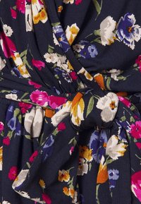 Dettaglio di un vestito a portafoglio floreale con sfondo blu navy e fiori multicolori, vita legata e tessuto morbido e testurizzato.