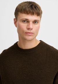 Bruine geribbelde gebreide trui met een ronde halslijn, met een gestructureerde afwerking en zachte uitstraling, gedragen door een model met kort haar.