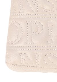 Materiale di colore crema con una texture prominente e lettering cucito in evidenza. Il design presenta testo audace, in rilievo, e dettagli di cucitura a contrasto.