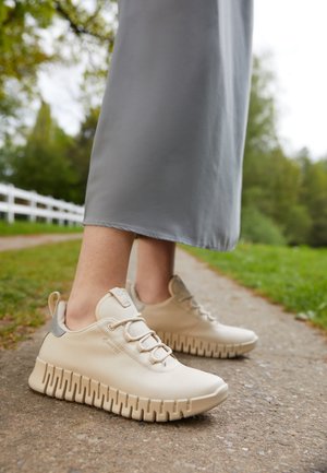 Kreeminväriset jooksukingad tekstureeritud nahaga, ümarate varvastega ja painduva, ribakujulise tallaga. Omab halli aktsenti ja nöörimise disaini.