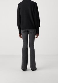 Schwarzer Strickpullover mit Rundhalsausschnitt und gepufften Ärmeln, kombiniert mit grauen, ausgestellten Jeans mit Gesäßtaschen und dezenten Nahtdetails.