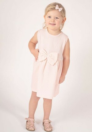 Jasnoróżowa sukienka bez rękawów z fakturowanej tkaniny, z dużą kokardą w talii. Połączona z sandałami w kwiatowy wzór.