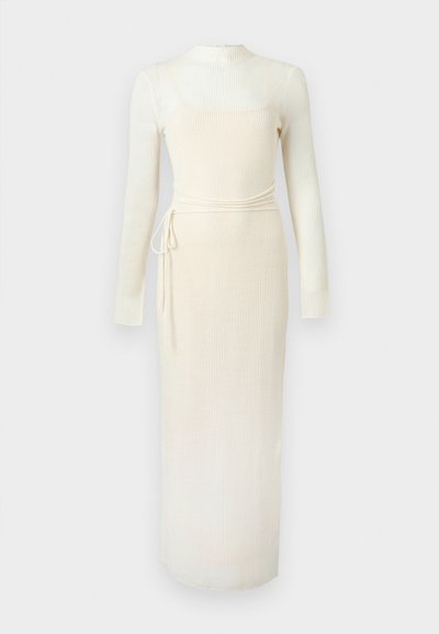 Robe longue en maille côtelée couleur crème, manches longues, col montant et fine ceinture à nouer sur le côté gauche.