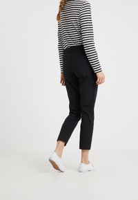 Černé kalhoty se zúženými nohavicemi a hladkou texturou, s páskem v pase a dvěma zadními kapsami, v kombinaci s černobílým pruhovaným topem a bílými teniskami.