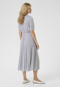 Gray, ribbed midi dress with a fitted bodice and flared pleated skirt. The model wears silver ballet flats. Simple round neckline.