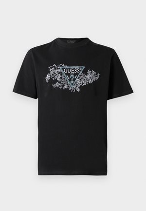 Svart bomulls T-skjorte med en trekantet "GUESS" logo i turkis, omgitt av hvit blomsterrikning, kortermet, og rund hals.