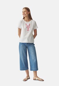 T-shirt en coton blanc avec un graphique de homard rose, associé à un pantalon large en denim bleu clair et des sandales à lanières.