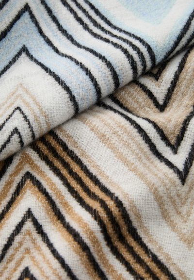 Kuosikangas, jossa on kevyesti sinisiä, beigejä ja mustia sahalaitamaisia viivoja valkoisella taustalla, pehmeällä, teksturoidulla kudoksella.