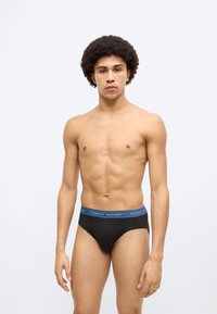 Μαύρα εσώρουχα με μπλε ζώνη μέσης που φέρει το λογότυπο "TOMMY HILFIGER", κατασκευασμένα από μαλακό ύφασμα, με εφαρμοστή γραμμή και μίνιμαλ σχεδιασμό.