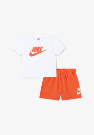 Tricou alb cu mâneci scurte Nike și logo portocaliu, asortat cu pantaloni scurți Nike portocalii cu talie elastică, cu logo alb pe picior.