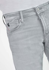 Lichtgrijze denim jeans met een klassieke vijf-pocketontwerp, subtiele stiksels, een zilveren knoop en een klein merketiket op de voorzak.