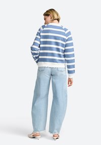Sweatshirt a righe blu e bianche con design cropped e orlo a costine, abbinato a jeans a gamba larga blu chiaro e mules bianche con tacco.