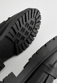 Black footwear with a textured leather upper and a thick, rugged rubber sole featuring deep treads and a flat profile.
