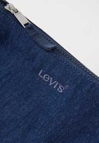 Midnattsblå denimväska med en silverfärgad dragkedja och präglad 'Levi's'-logotyp. Texturen verkar jämn med subtila tygvävdetaljer.