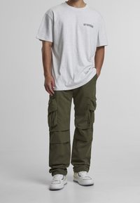 Camiseta gris de manga corta con logo negro, combinada con pantalones cargo verde oliva que cuentan con múltiples bolsillos y un corte relajado. Zapatillas blancas.