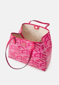 Roze Guess-tas met geometrisch patroon, dubbele schouderbanden, gouden logo en beige voering met herhalende merknaam.