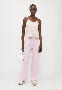 Beige sateng-camisole med tynne stropper, kombinert med lette, rosa vide bukser og en liten hvit håndveske med teksturerte detaljer.
