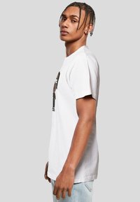 White cotton t-shirt featuring a character graphic on the front, short sleeves, and a crew neckline. Model is wearing light blue jeans.