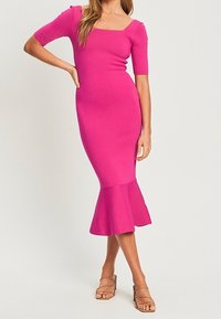 Abito rosa aderente a coste con scollo quadrato, maniche corte e orlo a campana. Indossato con sandali beige con tacco alto e fasce.