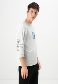 Lichtgrijs t-shirt met lange mouwen, gemaakt van katoen, met een blauwe grafische afbeelding op de borst en zwarte accentdetails op de mouwen.