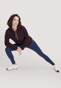 Burgunderfarbener Fleece-Pullover mit einem Halb-Reißverschluss-Kragen, kombiniert mit navyblauen Leggings und weißen Turnschuhen, der ein enganliegendes Design und eine glatte Textur zeigt.