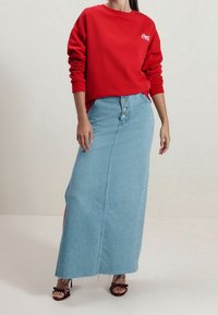 Rode sweatshirt met opgerolde mouwen en logo, gecombineerd met een lichtblauwe denim maxi rok met een voorste knoopsluiting en zijsplitten.