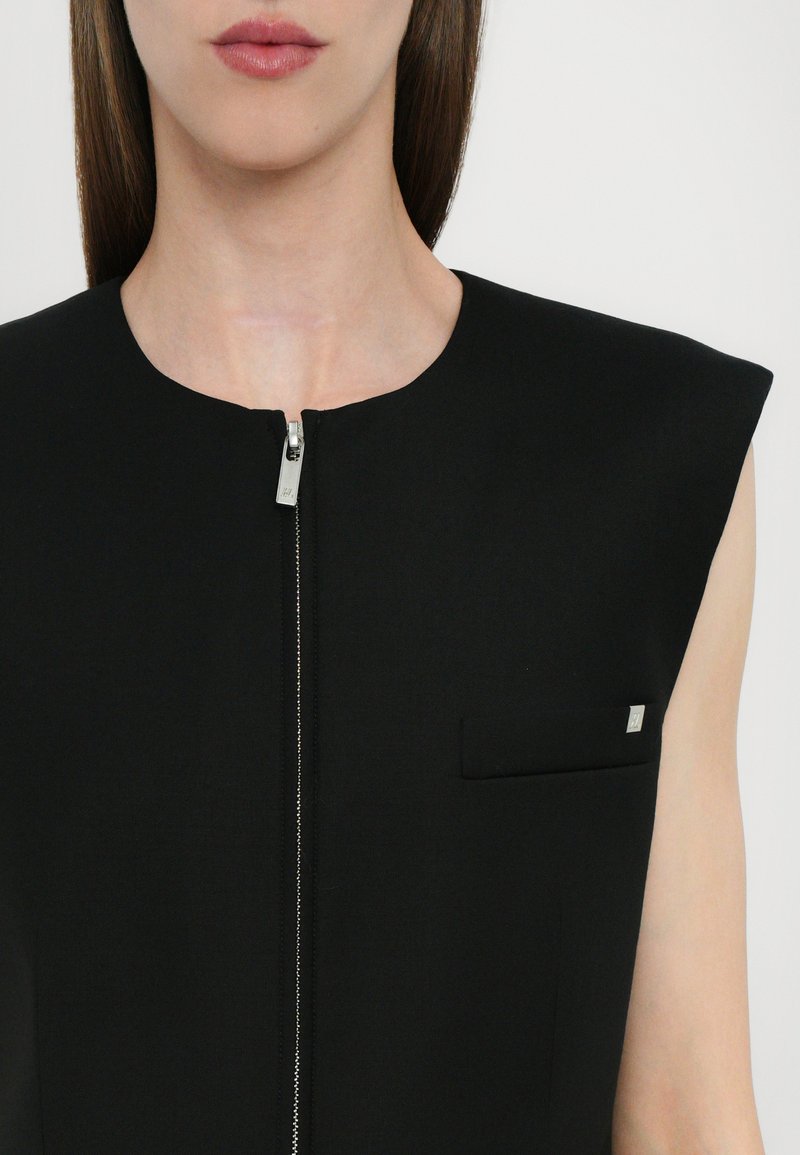 Black tailored dress featuring a round neckline, short sleeves, front zipper, and a small patch pocket with a silver accent.