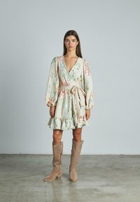 Blümchenmuster-Wickelkleid aus leichter Stoffqualität mit langen, gepufften Ärmeln und gerafftem Saum. Kombiniert mit beigen, mit Nieten verzierten Cowboy-Stiefeln.