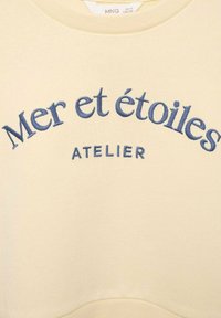 Sweatshirt girocollo di un delicato giallo pallido, con testo ricamato in blu "Mer et étoiles" e "ATELIER." Tessuto morbido con una texture liscia.