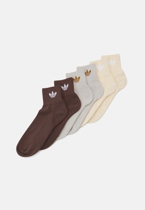 Pack of five ankle socks in brown, grey, cream, and light beige. Each features a ribbed cuff and a small logo on the ankle. Soft texture.