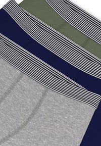 Τρία ζευγάρια ανδρικά εσώρουχα σε γκρι, ναυτικό μπλε και ελιά με ριγέ ελαστικές ζώνες στη μέση. Το ύφασμα φαίνεται λείο με απαλή υφή.