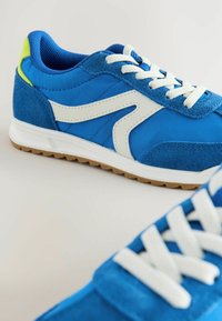 Baskets de sport bleues avec un mélange de matériaux lisses et en daim, accents blancs, lacets texturés et une semelle en caoutchouc durable.
