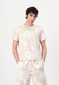 Lys beige t-skjorte med korte ermer og stort blomsterprint i lignende toner, laget av myk bomullsblanding. Har rund hals.