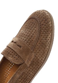 Mocassins en suede marron avec des perforations et une sangle assortie. L'intérieur présente une doublure lisse, améliorant la respirabilité et le confort.