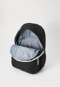 Mochila preta com um exterior suave e texturizado. A aba desfechada revela um interior forrado em cinza, com bolsos interiores e um acabamento liso.
